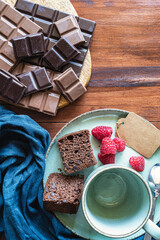Chocolate sponge cake with raspberries and chocolate bars on a rustic table.