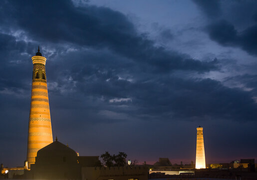 Night view of the Juma and Islam Khodja minarets illuminated in the old city of Khiva, Uzbekistan, highlighting the city's iconic Islamic architecture.