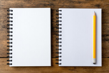 Blank spiral notebooks with white pages and yellow pencil on wooden surface, creating clean and organized workspace for writing or drawing ideas