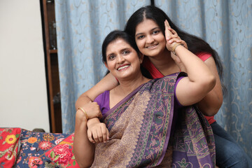 Portrait of happy young indian daughter mother hug each other at home, Sitting on her coach on sofa...