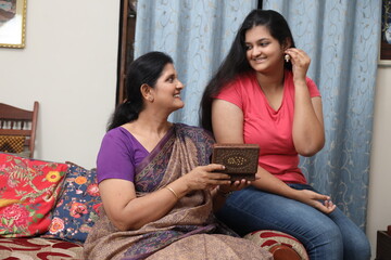 Indian woman gives a ear rings gift to her adult daughter as a gift. The woman wears the gold...