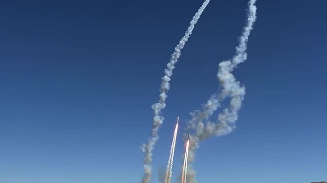 Rockets launching with smoke trails against a clear blue sky backdrop view