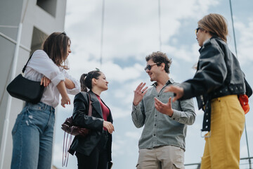 A group of casually dressed friends share a pleasant conversation outdoors. They stand together in...