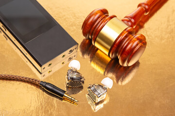 A pair of wired earbuds, a music player, and a gavel on a glossy golden background, symbolizing...
