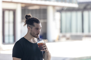 A handsome man in good body shape feels thirsty after fitness exercise. Young trainer is taking...