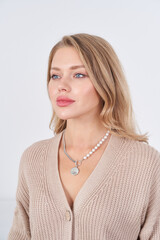 Woman with long blonde hair and blue eyes wearing a beige knitted sweater and a pearl necklace with...