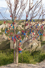 Wish tree decorating colorful small clay love pots and Blue Evil Eye pendants against blurred landscape of Love Valley in Cappadocia, Turkey
