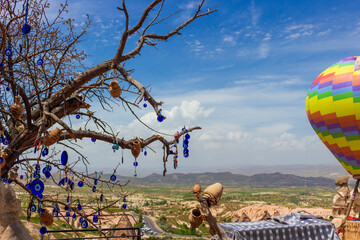 Colorful place for tourists with a hot air balloon, Evil Eye pendants and love clay pots in wish tree against blue sky at Uchisar in Cappadocia, Turkey