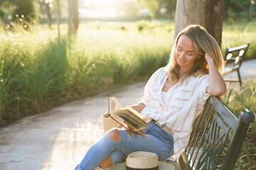 Woman reading book outdoors, relaxing on bench in summer park. Self-development in beautiful...