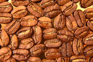 Close-up of roasted coffee beans on a lustrous golden tray, showcasing their deep brown color and intricate textures.