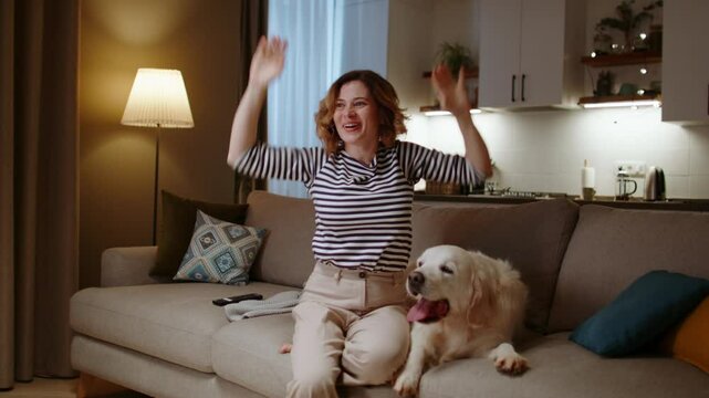 Woman cheers and high fives golden retriever after celebrating TV moment at home