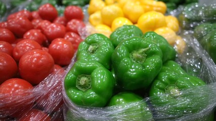 Close-up of ripe red tomatoes, glossy yellow bell peppers, and crisp green peppers packed in transparent plastic bags, glistening under sunlight at a bustling farmers market stall - Powered by Adobe