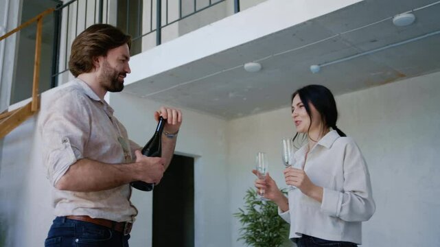 A joyful couple opens a bottle of champagne in their newly bought two-level apartment, celebrating the successful purchase of their dream home