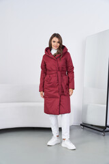Stylish woman in a red puffer coat with white pants and boots indoors