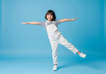 Obraz premium Playful Young Girl Balancing with Arms Outstretched on a Blue Background