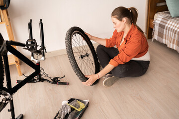 Young woman repairing bicycle holding wheel in home workshop, mechanic servicing the bike