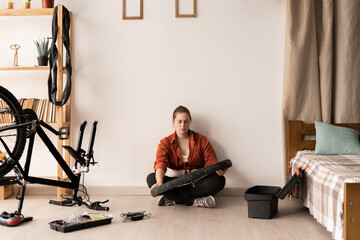 Young handywoman holding wheel from bicycle during a repair at home. Hobbies and DIY