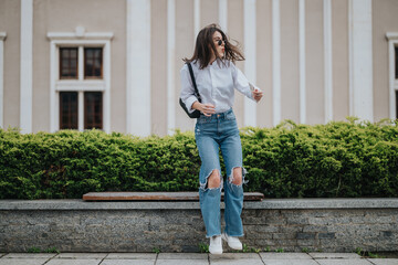 A young woman jumps energetically on a bench against a modern urban backdrop. Her confident style...