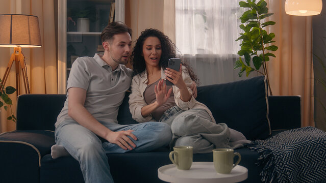 Multiracial happy couple family Caucasian man guy male Hispanic woman girl female talking using mobile phone together shopping online at home choose furniture goods purchase planning combined budget