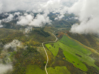 An aerial view captures a winding road traversing through misty, green mountainous terrain with...