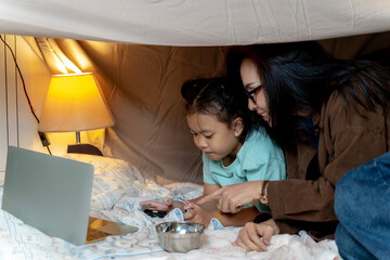 Joyful mother and daughter creating a cozy playhouse under the table, enjoying playful bonding time.