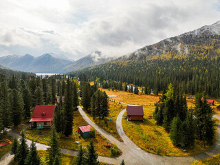 An aerial view of a serene mountain retreat featuring cabins by a lake, encircled by dense autumn...