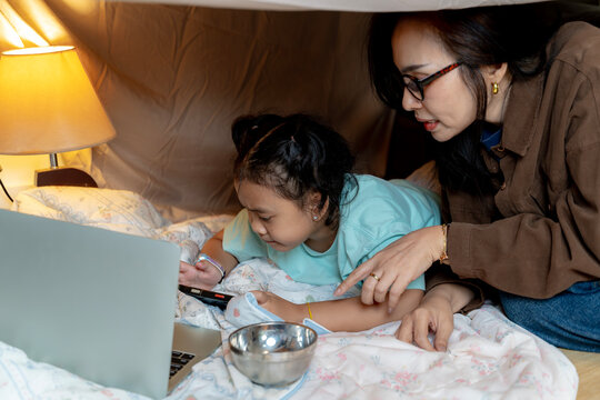 Joyful mother and daughter creating a cozy playhouse under the table, enjoying playful bonding time. - Powered by Adobe