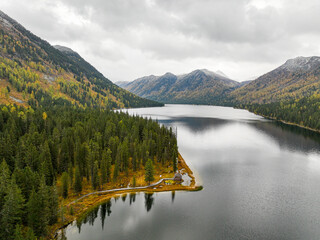 The serene shoreline of Rakhmanovskoe Lake, bordered by dense autumn forests, features a small boathouse and pathway
