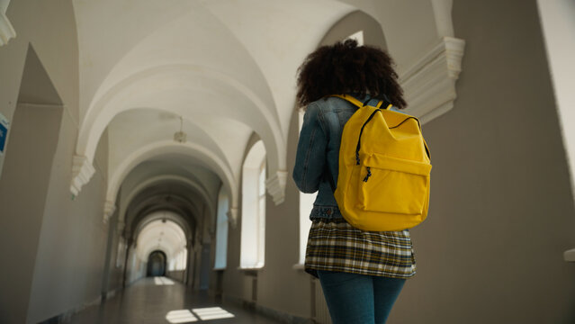 Empty corridor back view from behind student girl with yellow backpack follow going to class lesson in school university woman pupil female alone walking in academy college hall morning go to lecture