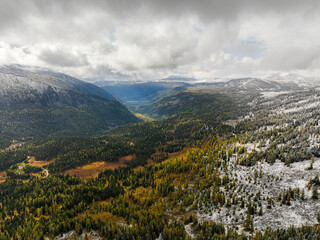 An aerial view shows a dramatic landscape where vibrant autumn forests transition into snow-covered...