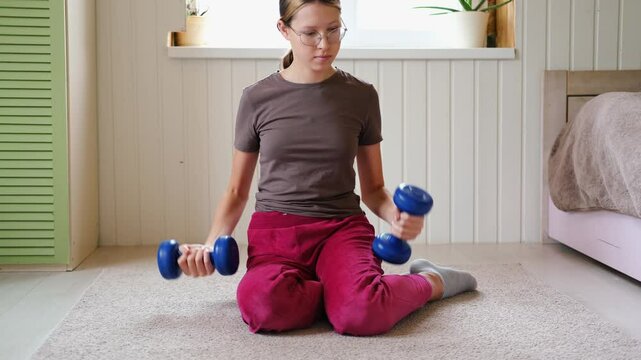 14 years old teenager customized workout, a mix of strength training, flexibility exercises, and cardio at home. Authentic shot. Teen girl exercises with dumbbells. Holistic Health, Mental WellBeing