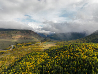An expansive aerial view of a valley showcasing dense autumn forests with green and yellow foliage,...