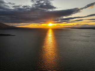 A vibrant sunset casts a golden glow over a vast lake, with the sun's reflection on the water and...