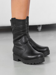 Black leather boots with thick platform soles and stitching details, worn by a person with the...