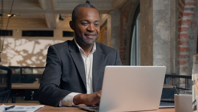 African American middle-aged entrepreneur smiling happy laughing positive typing laptop computer ethnic business man office businessman smile male guy working with pc online job chatting with client
