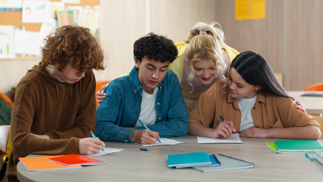 Four school Caucasian students pupils studying indoors male female prepare exams write homework teamwork learning men women girls guys teenagers writing discuss talking cooperation communicate friends