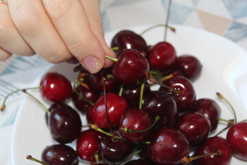 Person hand is picking cherry from many cherries in the bowl 