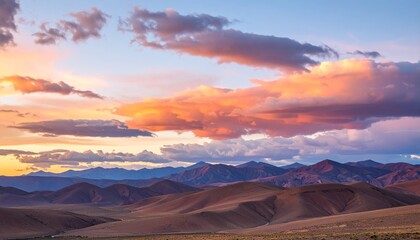 Naklejka premium Delicate pastel clouds stretch across a gradient sky, shifting from orange glow to soft midnight tones over smooth terrain. 