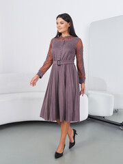 Woman in a flowing, long-sleeve dress with sheer lace details walks confidently. She wears black...