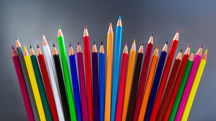 Fototapeta premium Colorful pencils arranged in a wave-like pattern, showcasing a spectrum of hues from yellow to green. Ideal for back-to-school, drawing, or artistic projects on a soft gray backdrop.