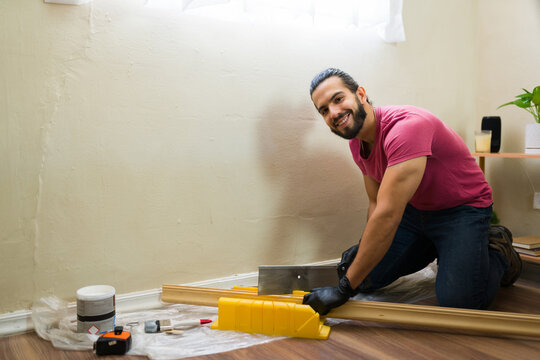 Hispanic contractor cutting wood trim using mitre box while installing baseboard at home