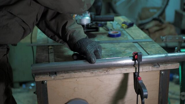 Workshop. The worker removes the clamps that were holding the cut steel pipe on the workbench and examines it.