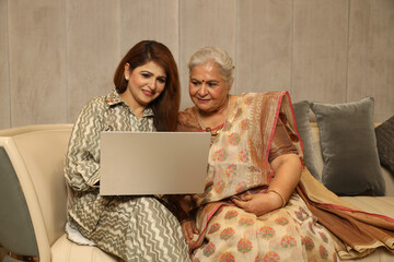 Indian happy young daughter  with her mother working on laptop. purchasing items through inline...