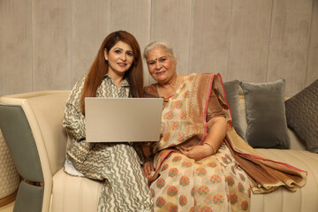 Indian happy young daughter  with her mother working on laptop. purchasing items through inline...