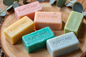 Colorful handmade solid soap bars stamped with 'Plastic Free' text, promoting a zero waste and sustainable lifestyle. Natural, eco-friendly beauty products on a wooden slice