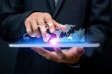 A businessman uses a tablet to analyze global market trends and data visualization showing worldwide economic growth and financial technology