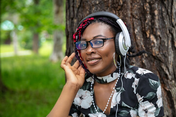 Happy African American Woman with Colorful Braids Listening to Music with Headphones in Park
