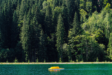 Yellow paddle boat floating on calm lake surrounded by lush green forest landscape