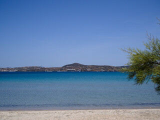 Tranquil Achivadolimni Beach on Milos island, Greece, with soft sand, turquoise sea, distant coast and Mediterranean tree under sunny sky.