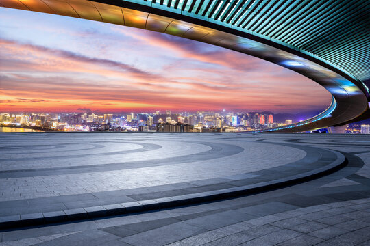 Empty circular square floor and bridge with illuminated modern city buildings at night